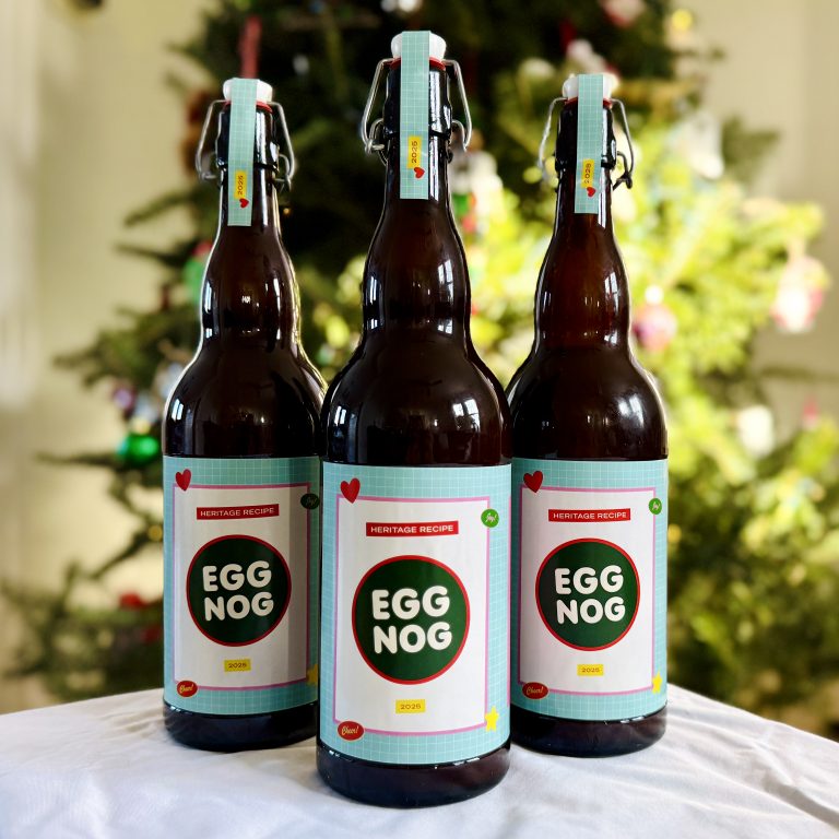 Three bottles of eggnog with retro-looking labels in front of a Christmas tree.